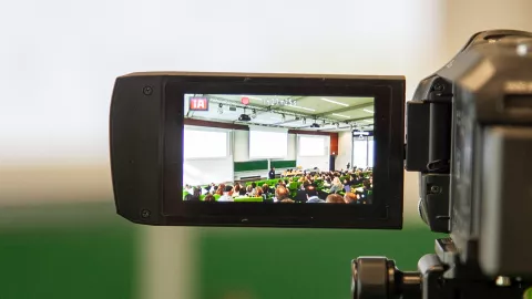 Blick in den vollen Hörsaal durch das Display einer Videokamera